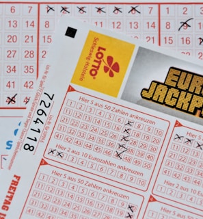 Three lottery tickets are displayed, including Eurojackpot and Super 6. Various numbers are marked on the tickets, with some crossed out and others checked. The Eurojackpot ticket is partially visible with the logo prominently displayed, and a ticket number is visible on one of the tickets.